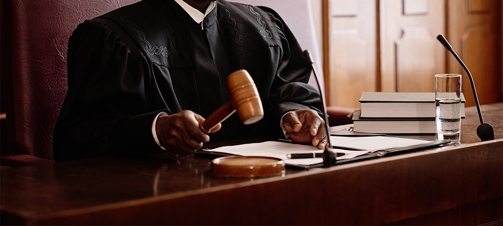 male judge with wooden gavel over sounding block sitting by desk