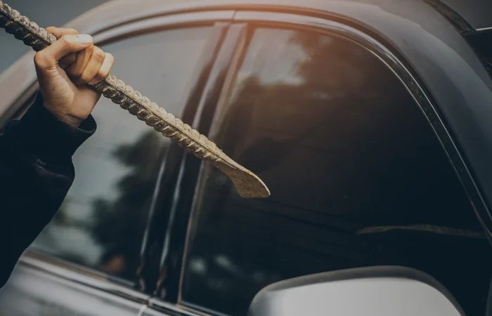 A robber dressed in black holding crowbar at a driver in a car. Car thief concept.