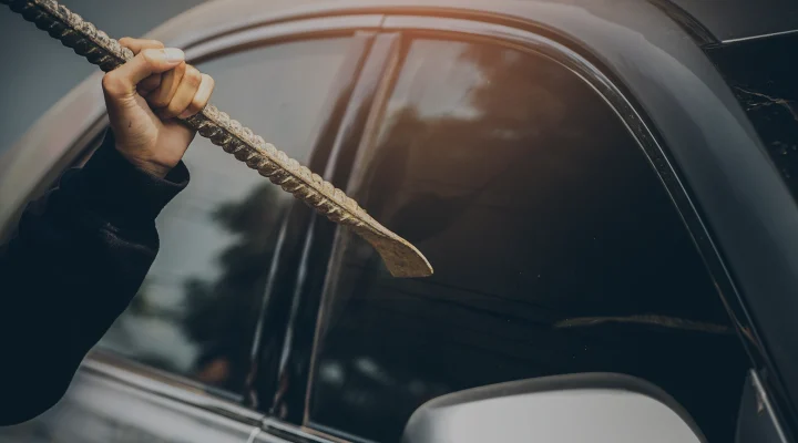 A robber dressed in black holding crowbar at a driver in a car. Car thief concept.