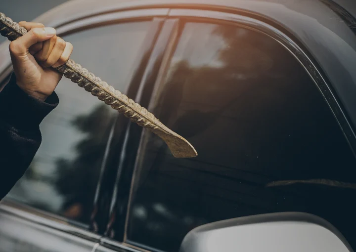 A robber dressed in black holding crowbar at a driver in a car. Car thief concept.