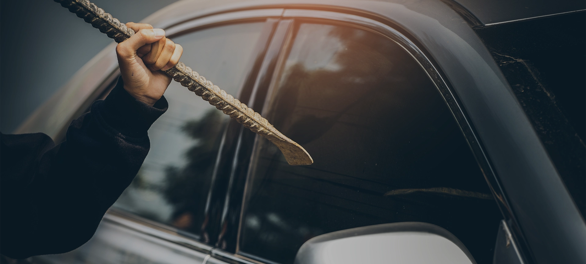 A robber dressed in black holding crowbar at a driver in a car. Car thief concept.