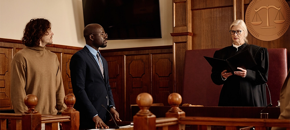 Confident female judge in black mantle standing in front of young intercultural attorney and suspect while passing judgement in courtroom