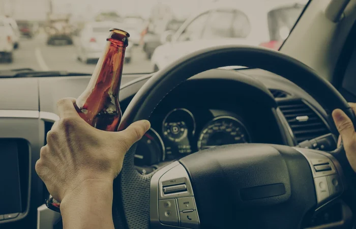 A driver holding alcoholic bottle while driving / Drunk driving concept