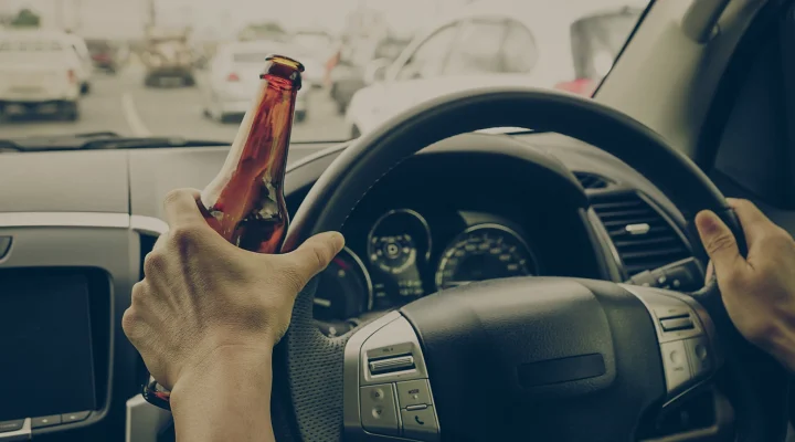 A driver holding alcoholic bottle while driving / Drunk driving concept