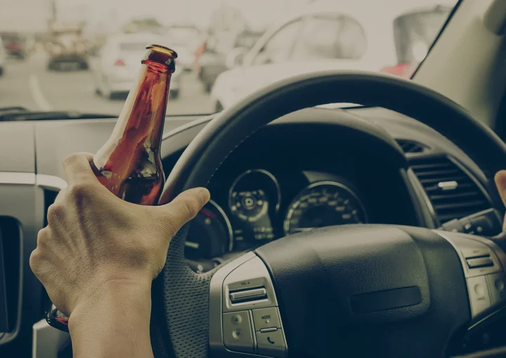 A driver holding alcoholic bottle while driving / Drunk driving concept