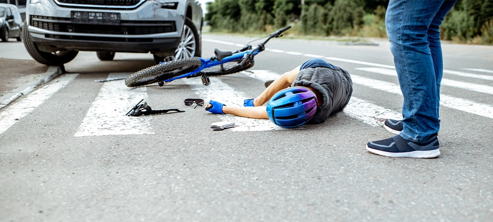 Scene of a road accident with injured cyclist lying on the pedestrian crossing near the broken bicycle and car