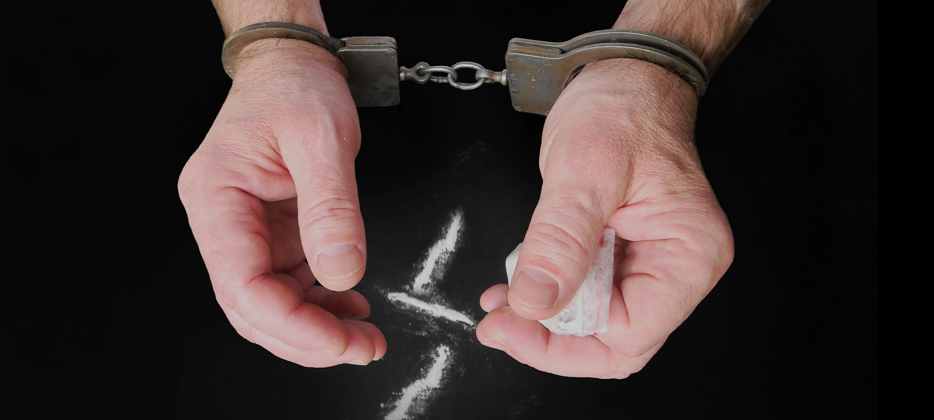 Police handcuffs on men's hands, heroin, cocaine powder and a bag of the substance. Punishment for drug distribution.