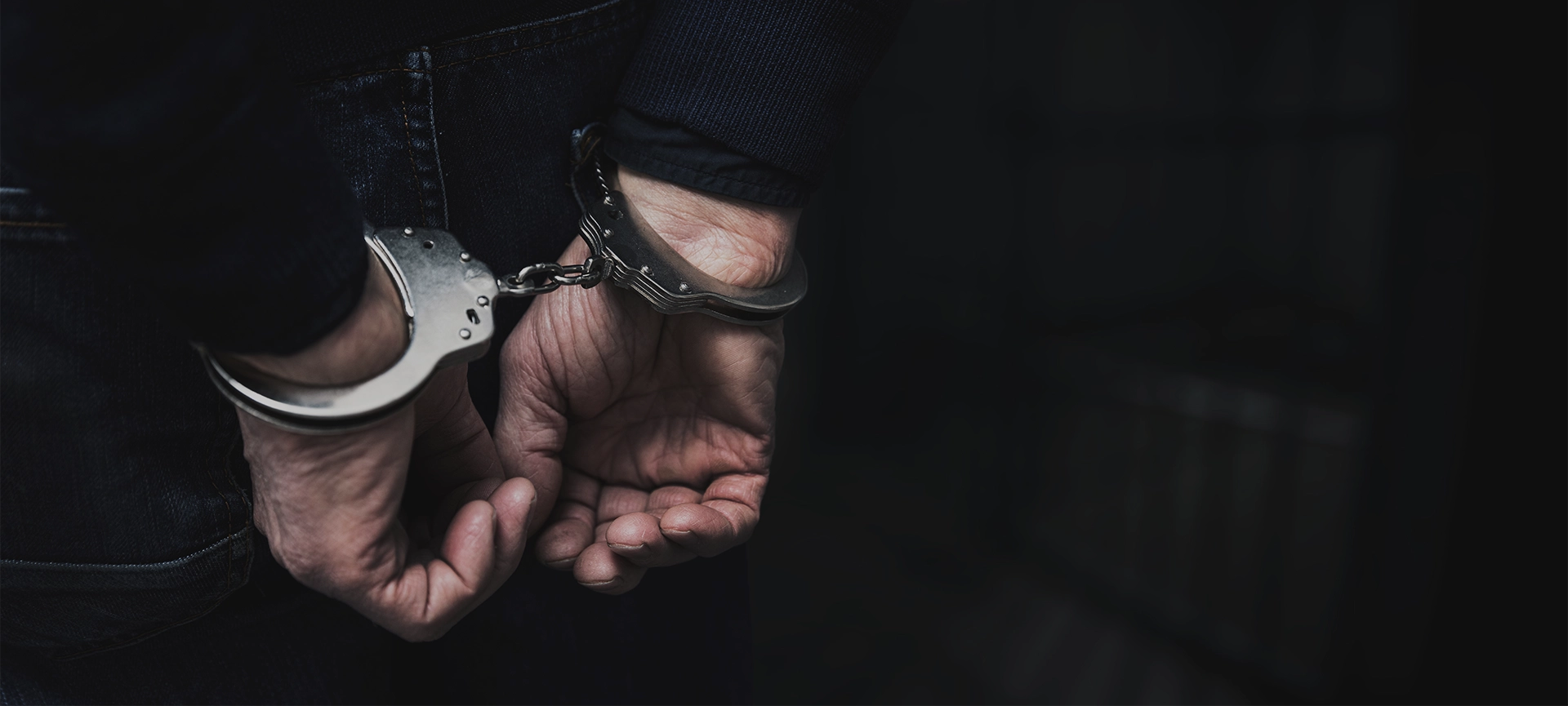 handcuffed arrested man behind prison bars.