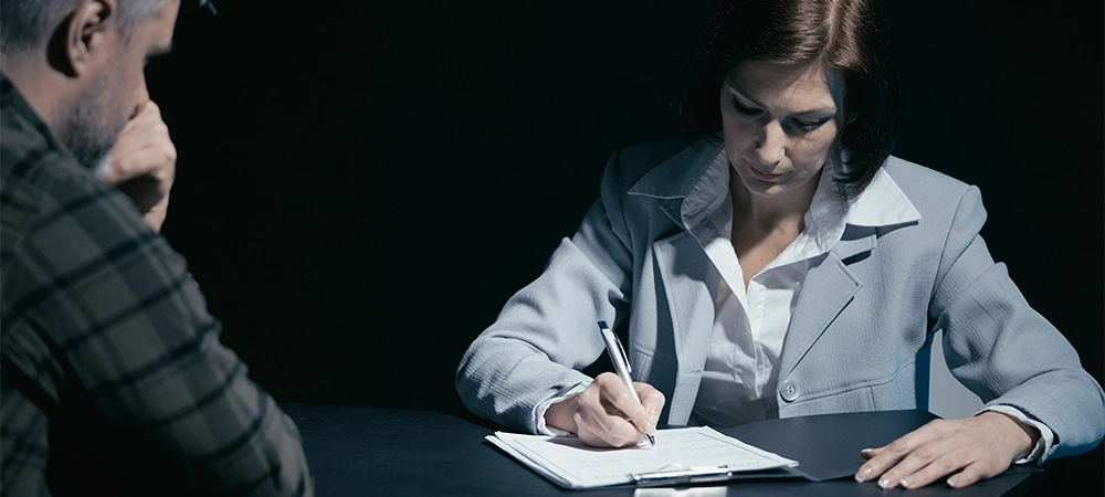 Suspected man talks to his lawyer, who is making notes in the interrogation room