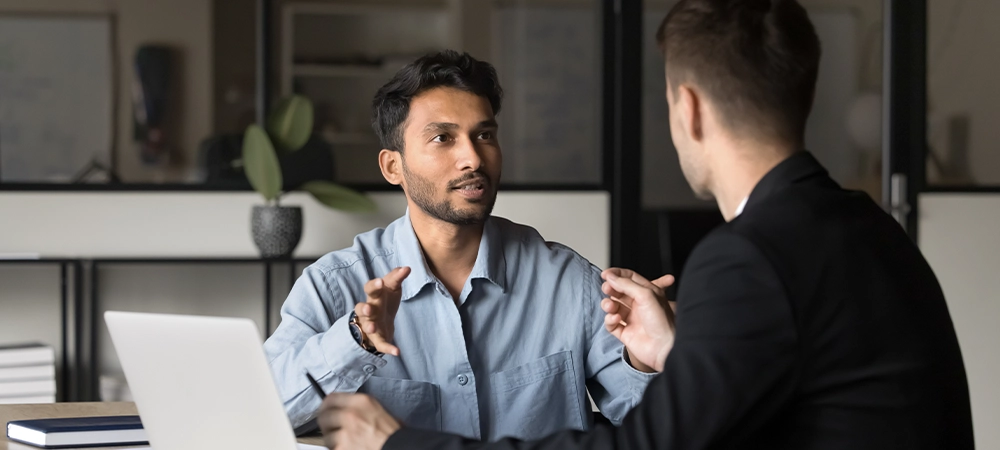 Two diverse businesspeople lead collaborative discussion in corporate boardroom. Busy handsome CEO executive Indian manager speaks, consulting, sharing expertise and insights with colleague or client
