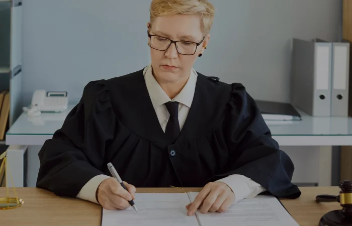 Judge serious woman in professional outfit black robe writing reviewing documents in court room at desk, examination, discussion of legal and judicial settings, lawyer consultation, case preparation